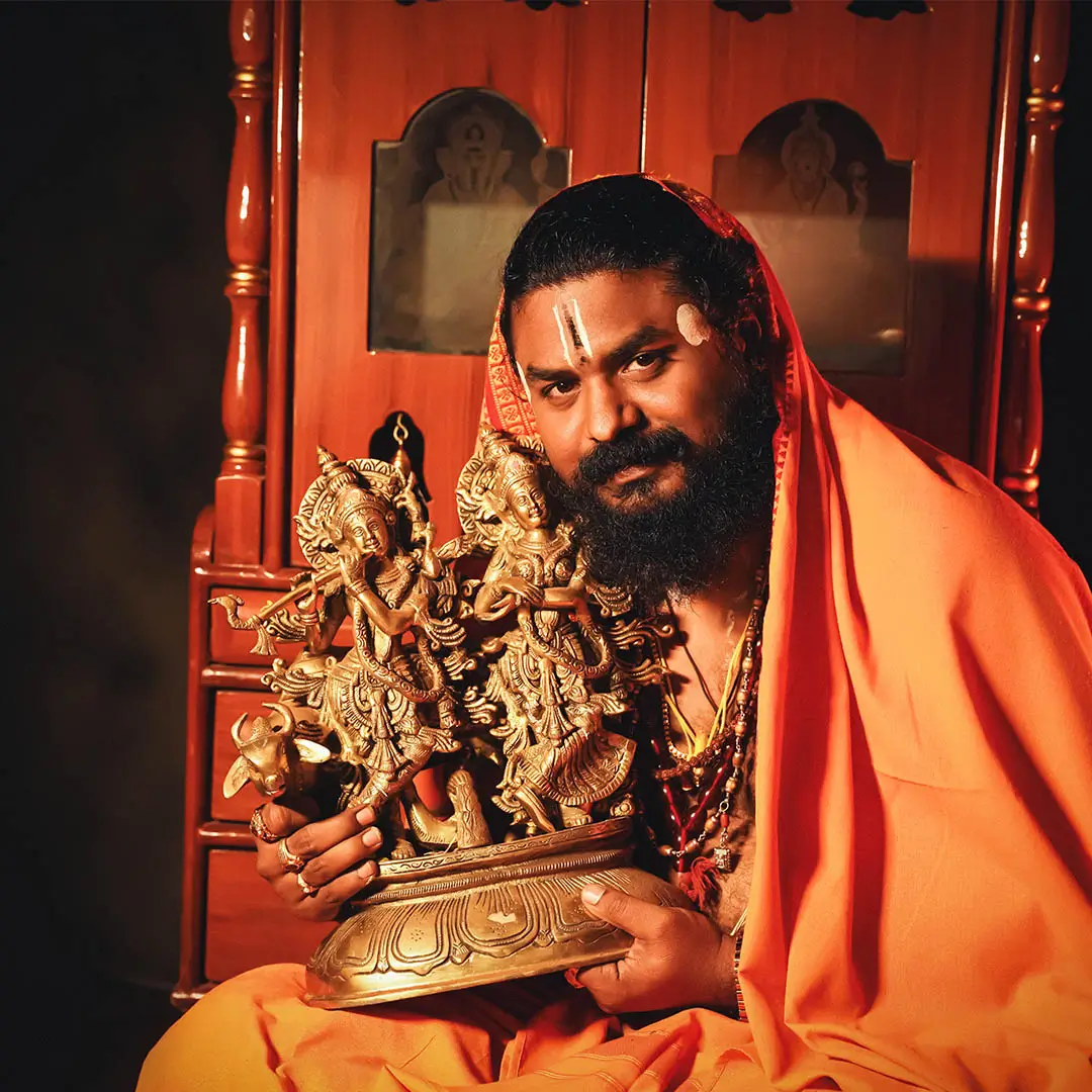 Dr. Pandit Sri Sidhant Arun Sharma Guruji at his shrine, holding a brass idol of Krishna and Radha